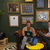 Twee developers zitten op een bank met een laptop op schoot en zijn aan het overleggen.