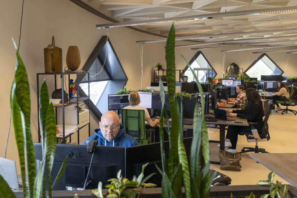 Een overzicht aan alle werkplekken op kantoor met enkele collega's die aan het werk zijn op hun laptop.