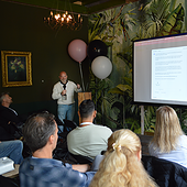 Bedrijfspresentatie door Sturdy Digital met een grote scherm en een groep professionals in een sfeervolle, groene ruimte met tropische planten en ballonnen.
